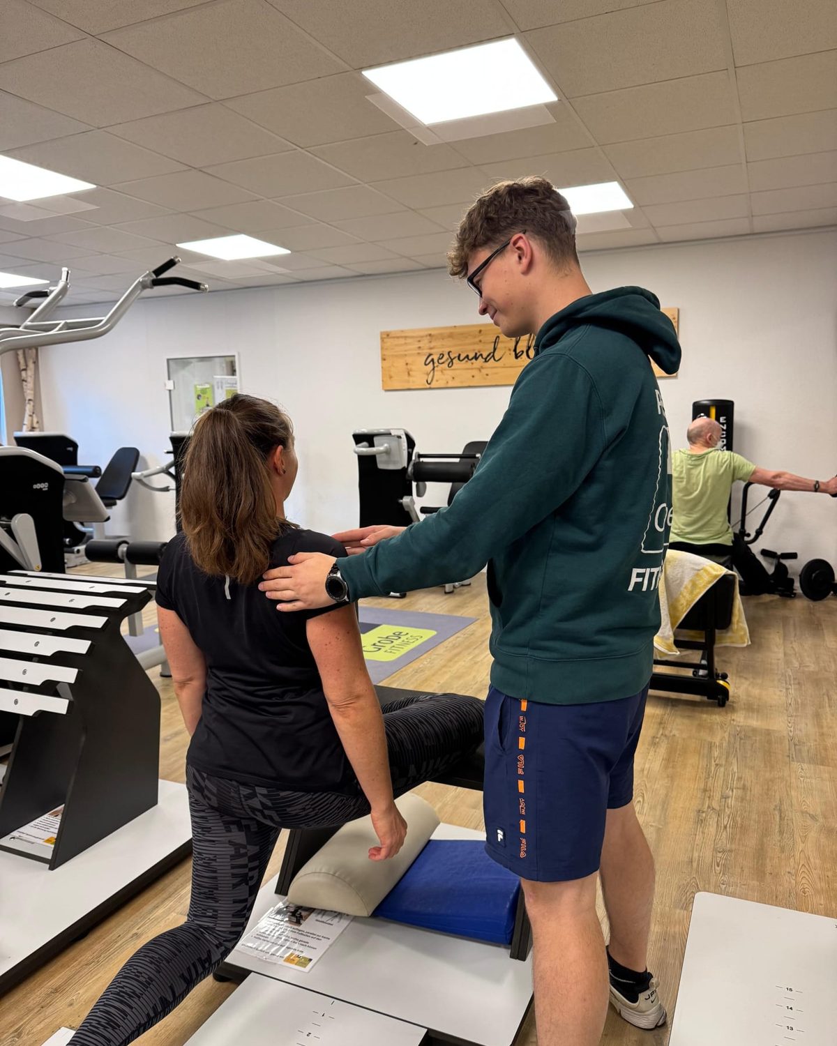 Trainer korrigiert die Haltung eines Mitglieds an einem Trainingsgerät